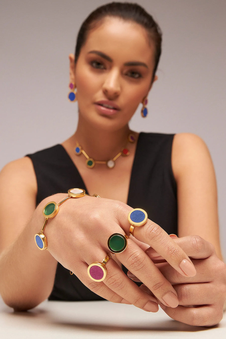 Modelo de vestido preto usando anéis, pulseira e colar da linha Eterno em várias pedras coloridas, banhados a ouro 18k