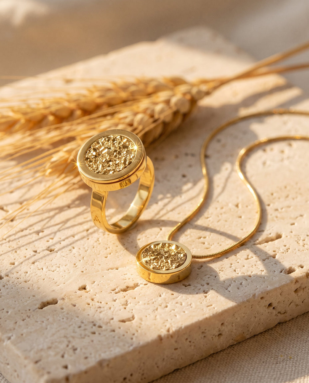 Anel Eterno e Colar Eterno com Drusa Ouro, banhados a ouro 18k, sobre travertino ao sol, com espigas de trigo secas